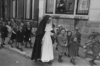 221117 Afbeelding van een kleuterklas van de St.-Dominicusschool (Alendorpsteeg) onderweg onder leiding van zuster ...